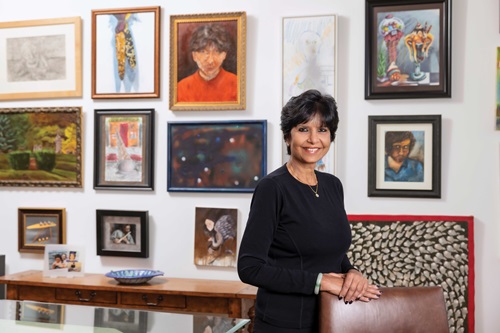 Usha Raj, MD, MHA, FAPS, stands in front of a wall of framed art pieces