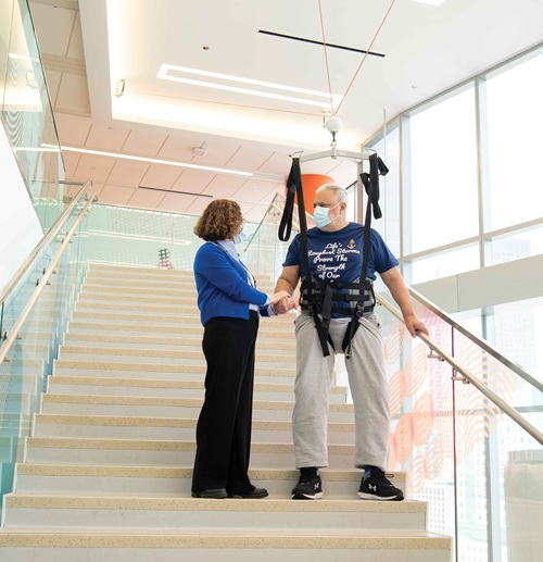 Feature-art_Dr-Perez_4 Perez stands on with a patient wearing a harness to help them on a stairwell
