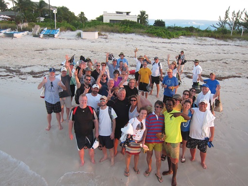 about forty people stand together on a beach and wave to a camera