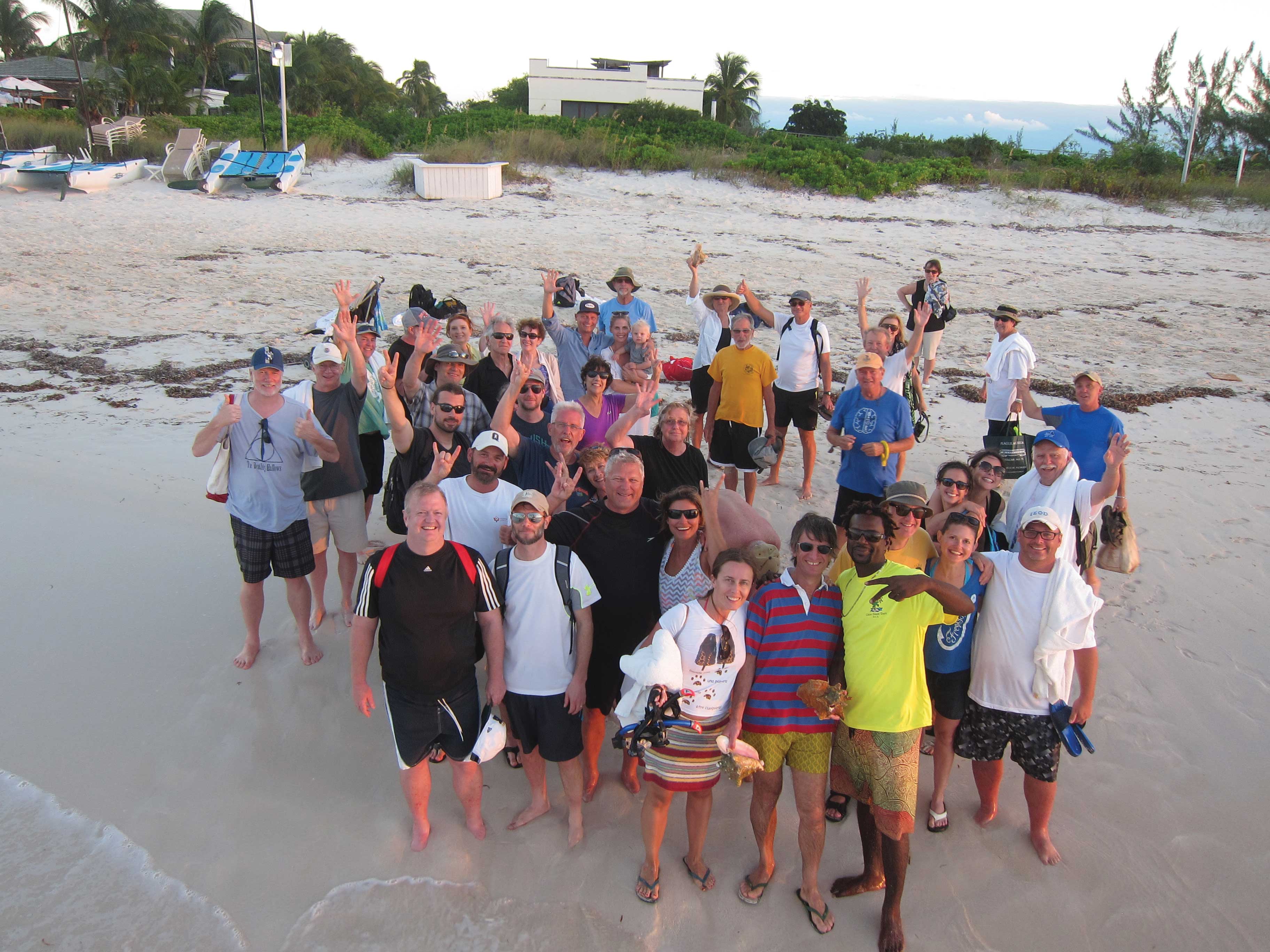 about forty people stand together on a beach and wave to a camera