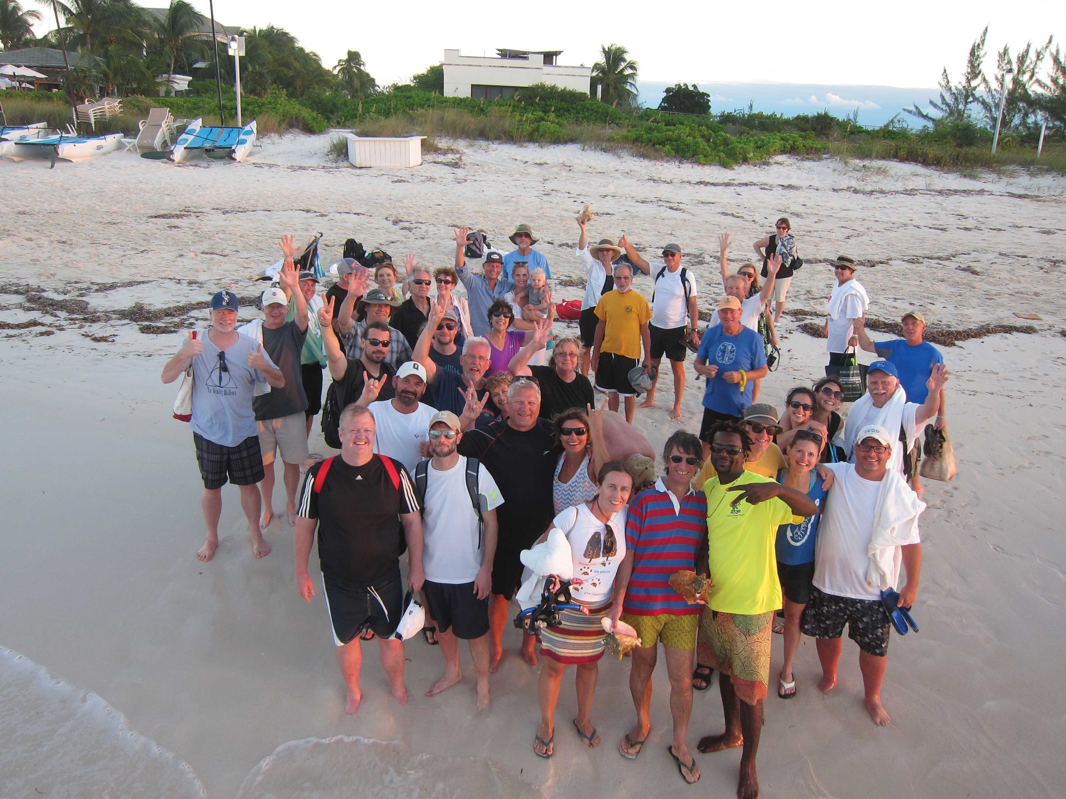 Feature_Samson_Photo-2 about forty people stand together on a beach and wave to a camera
