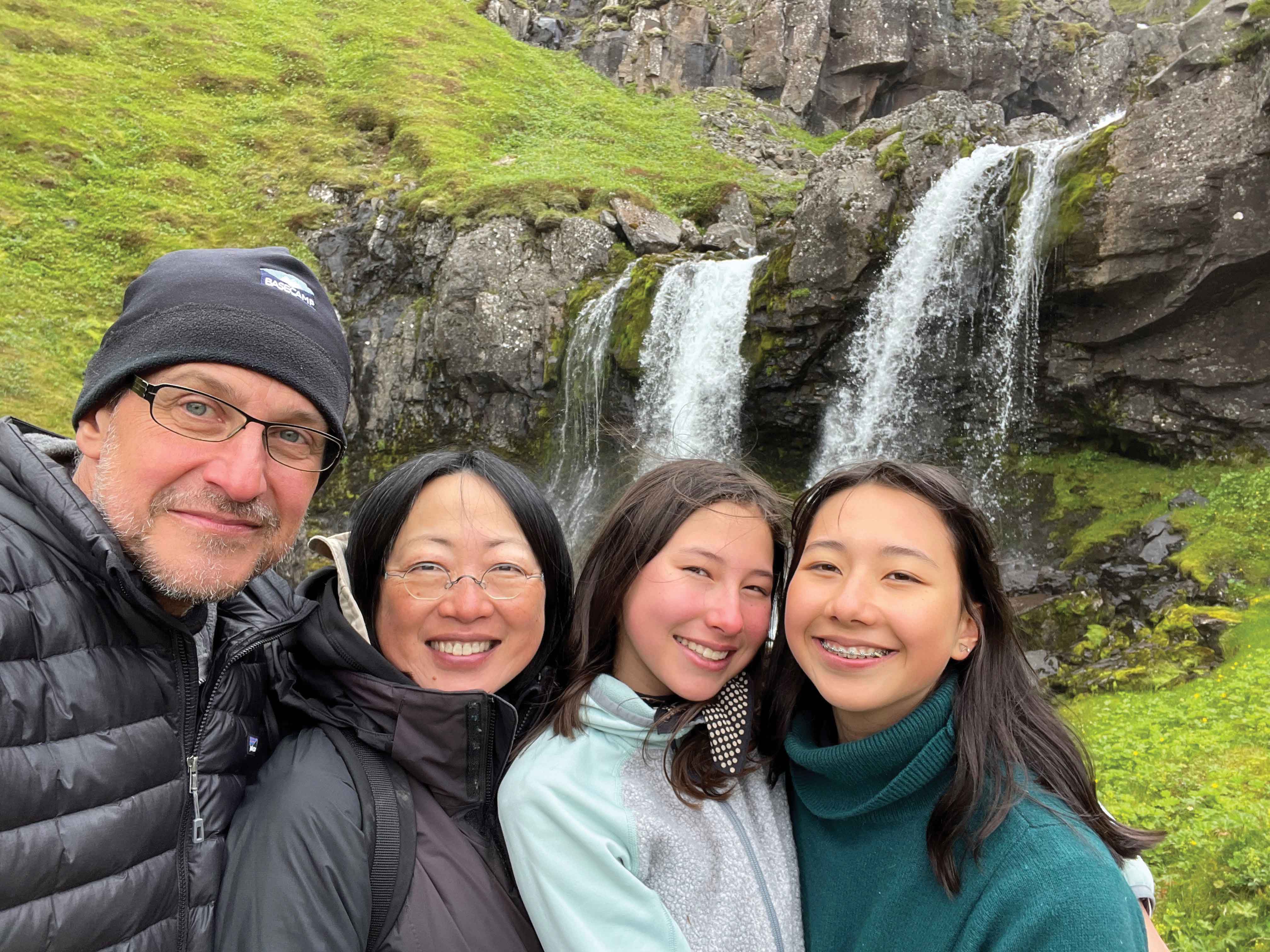 a family of four smile in front of a waterfall